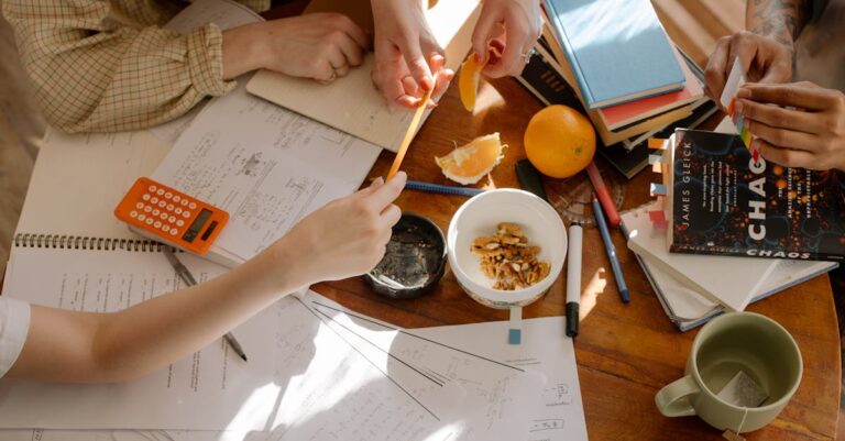 Grupo ao redor de mesa com mapas mentais e rascunhos, discussão em ambiente universitário.