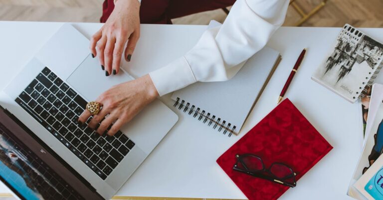 Mãos digitam carta de apresentação no laptop com bloco de notas ao lado