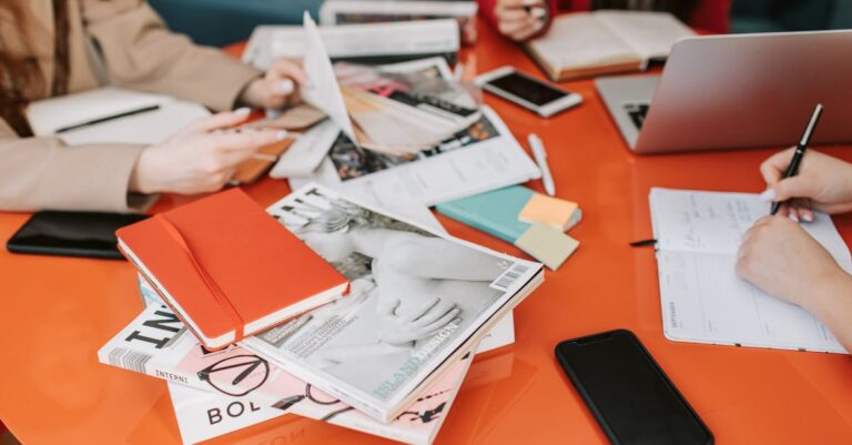 Mãos e laptops sobre mesa com papéis e pautas, grupo preparando trabalho acadêmico