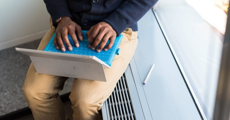 Mãos digitando e‑mail curto no laptop, com caderno e caneta ao lado, vista superior.
