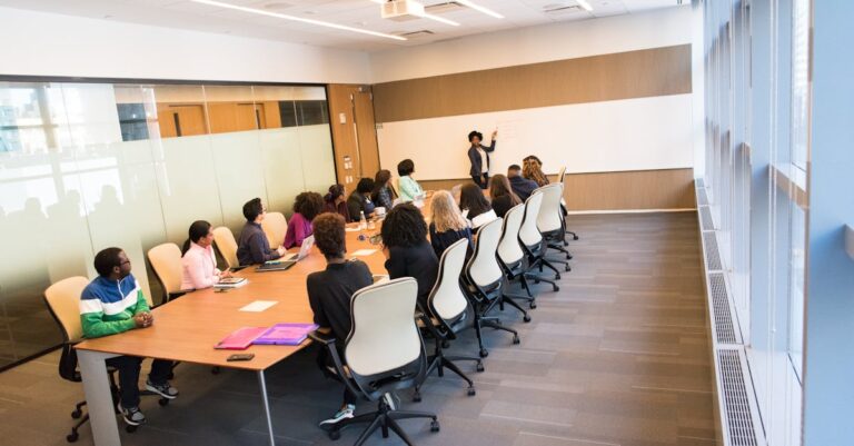 Pequeno grupo reunido em sala universitária, quadro branco com organograma e pessoas discutindo planos.