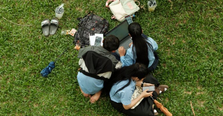 Pessoa ensaiando fala diante de smartphone e laptop, roteiro visível e equipamento de gravação na mesa.