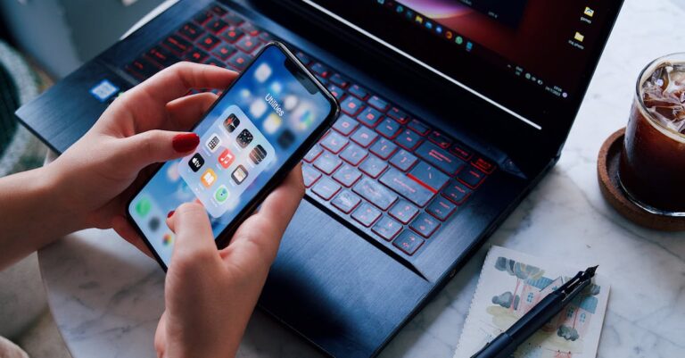 Smartphone com rascunho de email e laptop ao fundo, mãos segurando o aparelho.