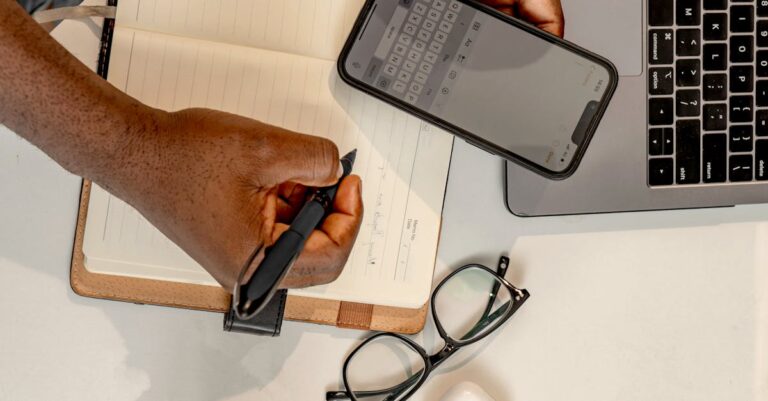Mãos no teclado do laptop com cronômetro no smartphone e notas impressas, ensaio cronometrado.