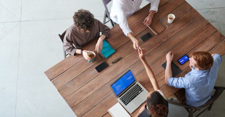 Pequeno grupo ao redor de mesa com laptops e cadernos trocando feedback de escrita