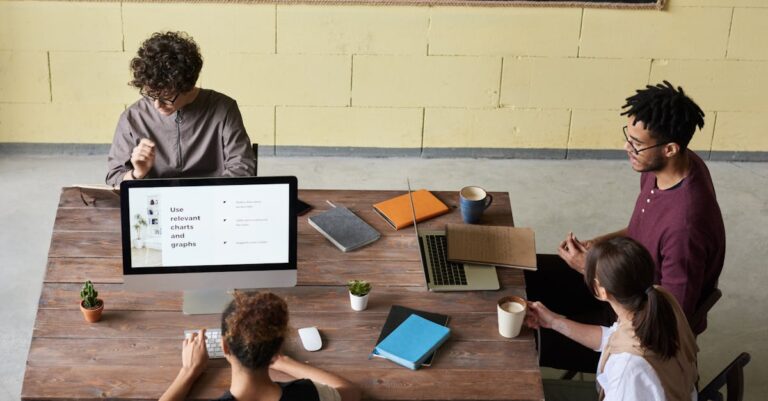 Duas pessoas revisando manuscrito no laptop, checklist em prancheta sobre a mesa