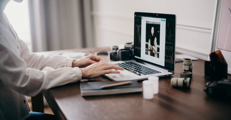 Mãos digitando em laptop com janela de chat aberta e anotações ao lado
