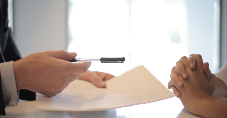 Manuscritos e documentos institucionais sobre mesa com mãos segurando caneta, simbolizando políticas e autorizações.
