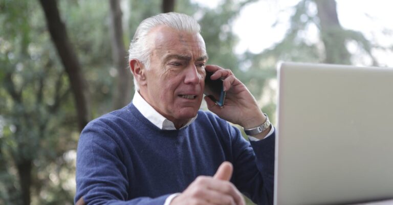 Laptop e smartphone com notificações e alertas, mãos segurando o telefone para checagem