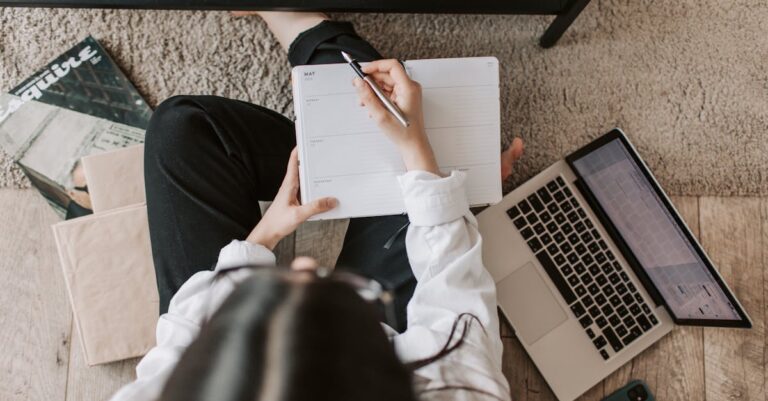 Planilha aberta no laptop, aplicativo de controle de tempo no celular e caderno ao lado, visão superior