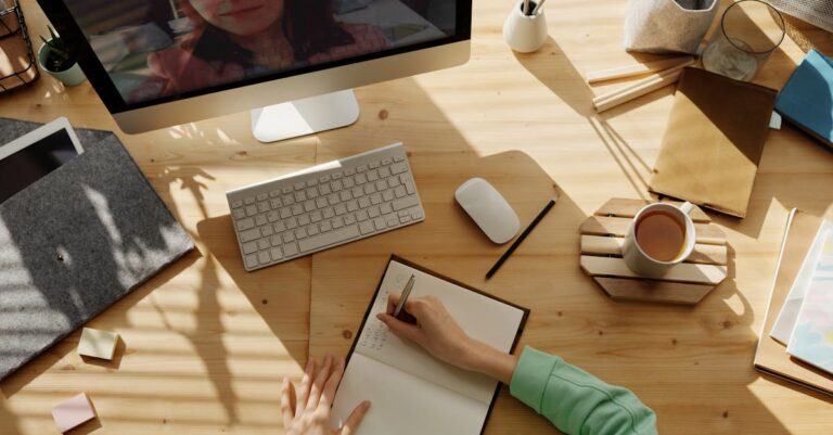 Duas pessoas escrevendo juntas, mãos sobre cadernos e laptop aberto, representando sessão de responsabilidade mútua.