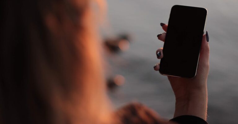 Mãos no teclado e smartphone enquanto PDFs e um formulário de inscrição aparecem na tela do laptop.