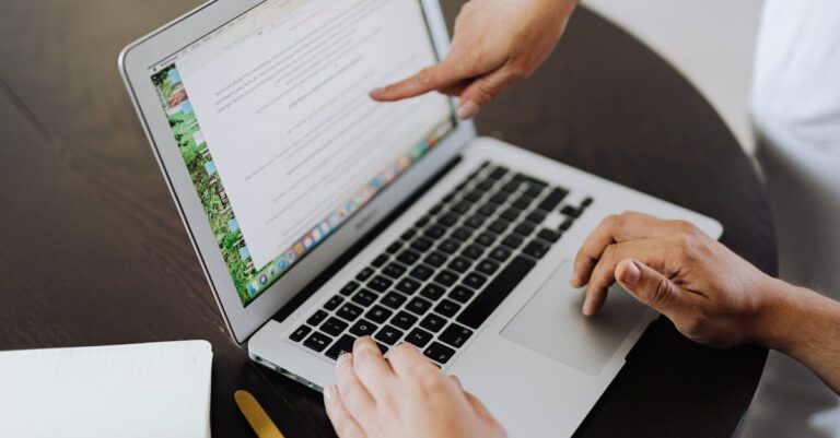 Mãos apontando para tela de laptop com rascunho e anotações durante revisão colaborativa