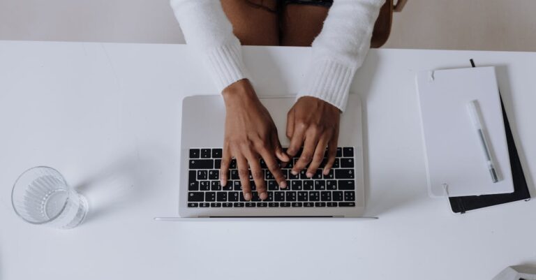 Mãos no teclado com tela de exportação de PDF ao fundo e páginas impressas ao lado