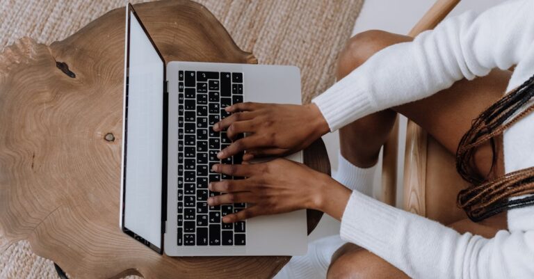 Mãos digitando em laptop com checklist e PDFs de inscrição abertos na mesa
