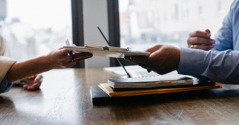 Mãos trocando documento sobre mesa com laptop aberto, simbolizando negociação de prazos