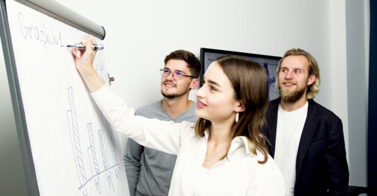 Mãos apontando para quadro com diagramas enquanto duas pessoas discutem abordagem interdisciplinar