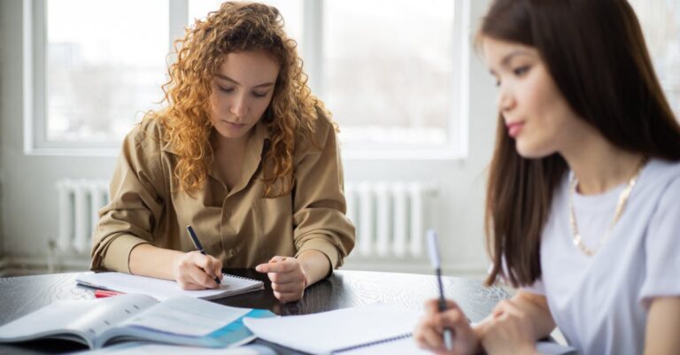Colegas escrevendo e trocando feedback em sessão de escrita guiada, com laptops e anotações visíveis