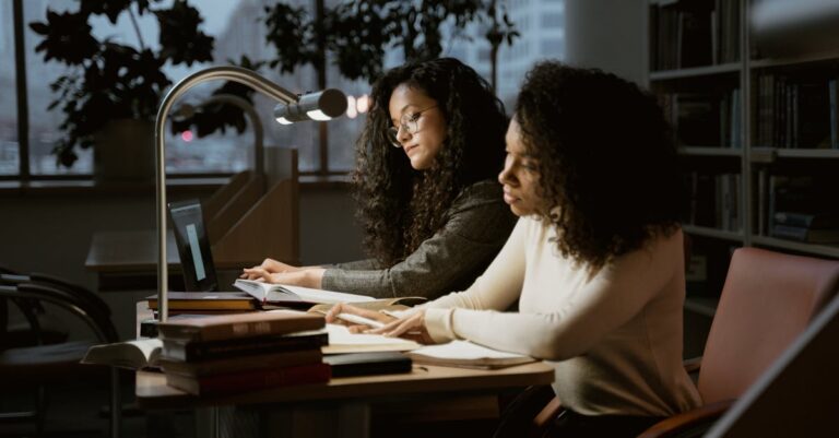 Mãos apontando para tela de laptop em biblioteca com estantes ao fundo