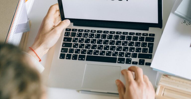 Mesa com laptop e papéis amassados, sugerindo frustração e erros comuns na escrita acadêmica.