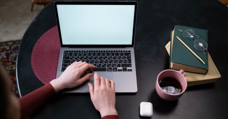 Mãos digitando e-mail de follow-up em laptop com xícara de café ao lado.
