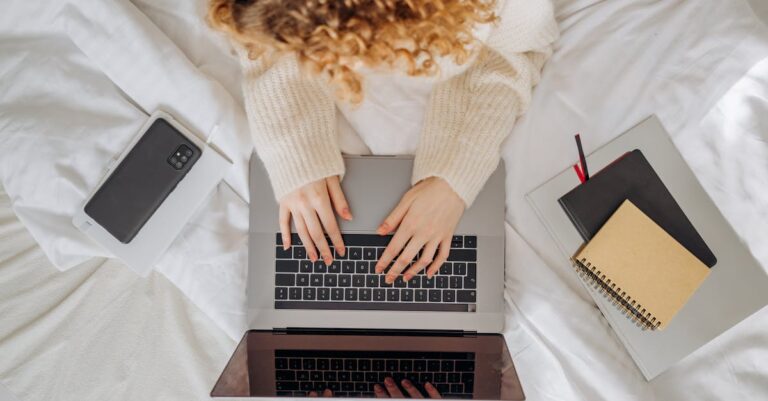 Mãos digitando em laptop com editor de texto aberto e notas ao lado, representando revisão assistida