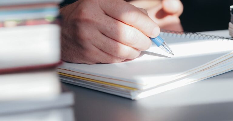Mãos escrevendo uma lista de tarefas em caderno, com cronômetro ao lado, destacando detalhamento e tempo.