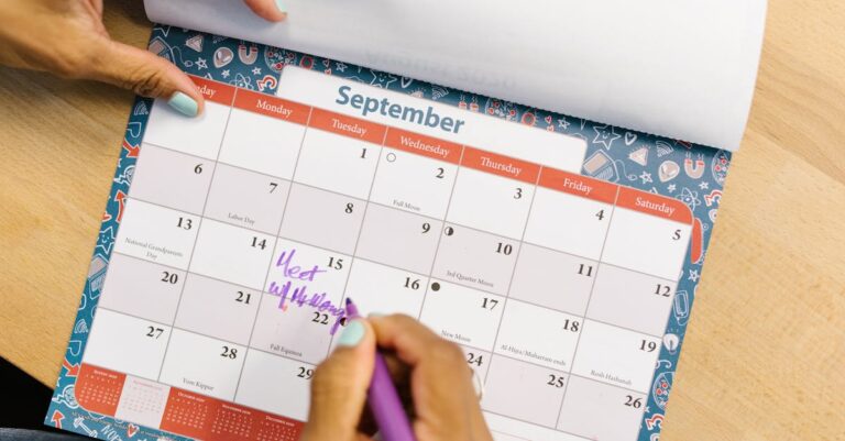 Mãos marcando datas num calendário ao lado de laptop e checklist sobre mesa