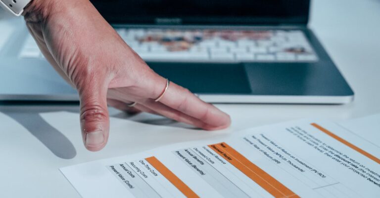 Mãos apontando para artigos impressos e laptop sobre a mesa, revisão coletiva de evidências e diretrizes.