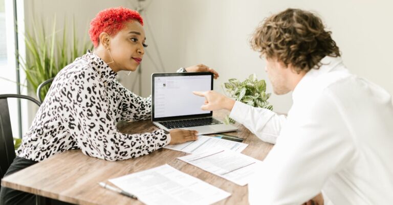 Mãos apontando para rascunhos impressos e laptop durante revisão entre colegas