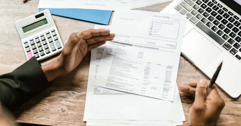Mãos usando calculadora sobre planilha orçamentária, laptop e anotações ao lado