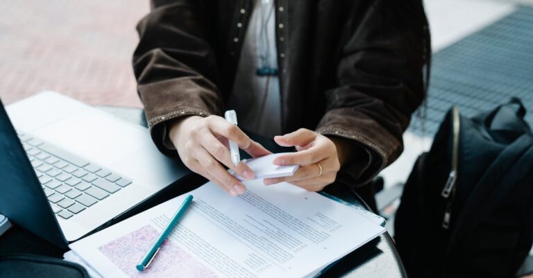 Mesa de reunião com documentos, laptop e anexo, preparação para responder à banca