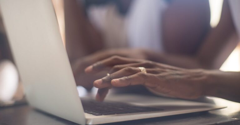 Mãos digitando em teclado com texto destacado na tela, sugerindo vigilância e revisão ao usar IA