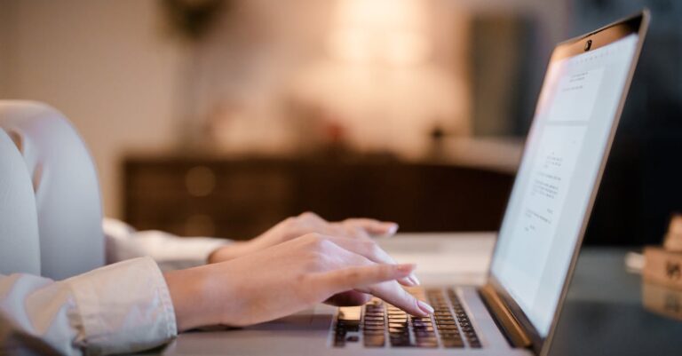 Mãos sobre teclado e documentos de privacidade ao lado do laptop, indicando avaliação de segurança de ferramentas