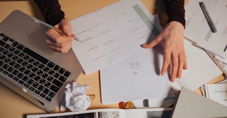 Mesa vista de cima com laptop, rascunho impresso e marcador, mãos avaliando sugestões de texto
