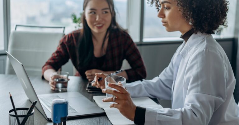Pessoa praticando apresentação com laptop, anotações e cronômetro, simulando arguição.