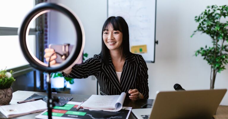 Smartphone em tripé gravando breve apresentação, com laptop e material de apoio ao fundo