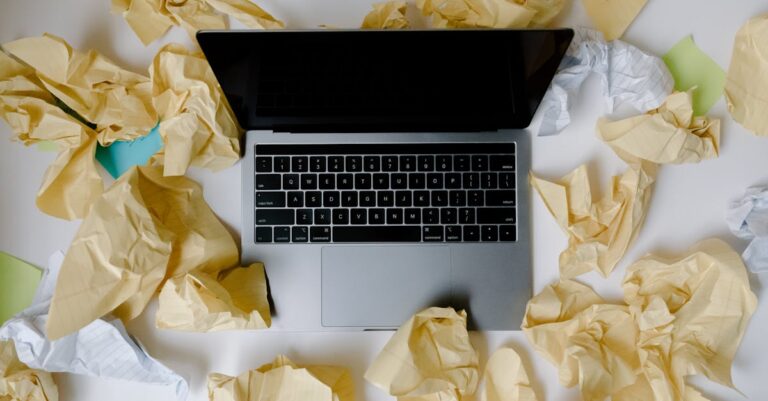 Folhas amassadas, notas riscadas e laptop com outline desorganizado sobre a mesa