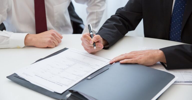 Mãos assinando acordo de autoria sobre mesa com documentos, reunião discreta entre coautores