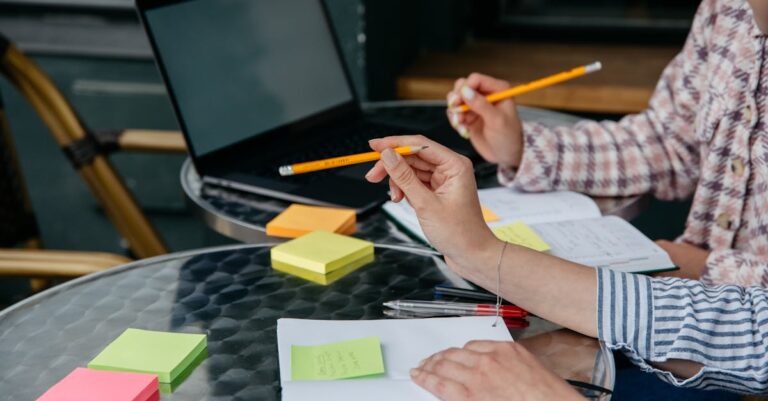 Mãos sobre caderno e laptop durante conversa, gesto de negociação em ambiente de escritório