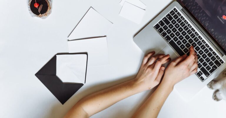 Mãos digitando no laptop com documentos e checklist ao lado, vista superior