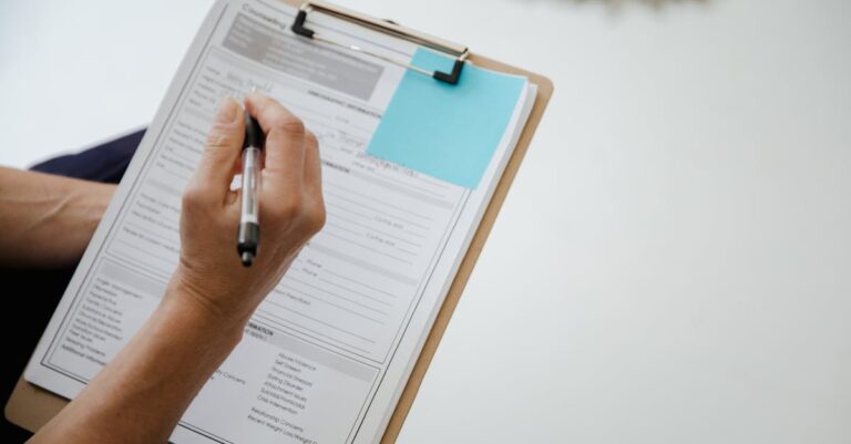 Mãos digitando inscrição on‑line em laptop, com checklist e documentos ao lado sobre a mesa.