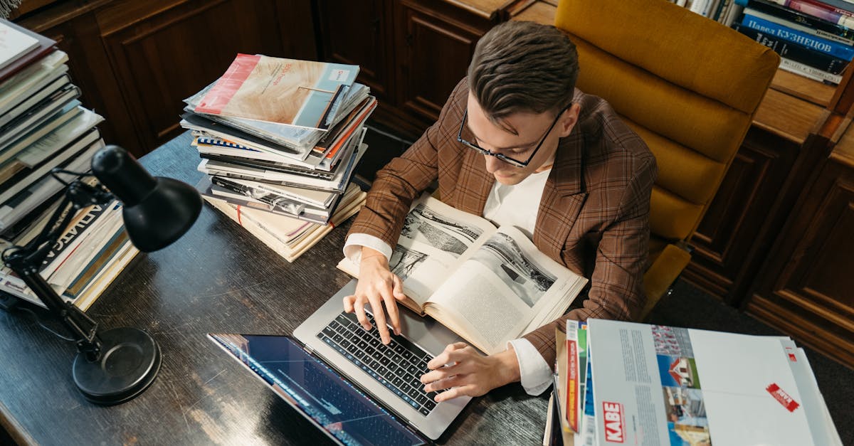 Mãos digitando num laptop com papéis de pesquisa e um cronômetro sobre a mesa de estudo