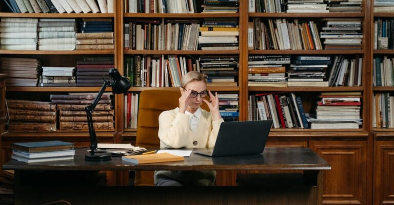 Computador em ambiente de biblioteca com artigos e pilhas de periódicos, sugerindo busca por repositórios e normas