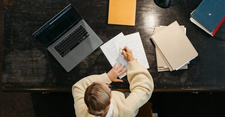 Pessoa comparando três versões de um parágrafo no laptop, com notas e marca‑texto sobre a mesa