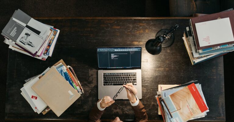 Pessoa escrevendo e-mail no laptop com livros e anotações numa mesa de biblioteca
