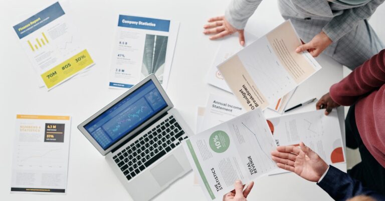 Pesquisadores e servidores públicos revisando relatórios sobre a mesa, com laptops e papéis organizados