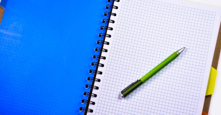 Pesquisador anotando em caderno com laptop ao lado, simbolizando economia de tempo em tarefas bibliográficas