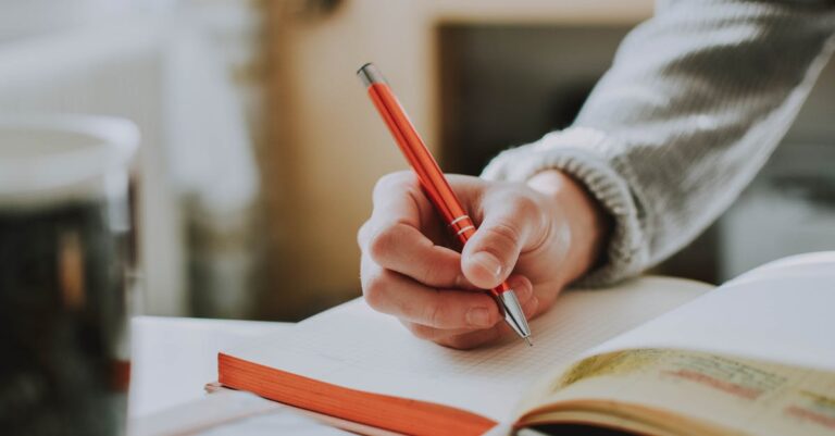 Mulher pesquisadora escrevendo anotações de campo em caderno aberto com fundo neutro