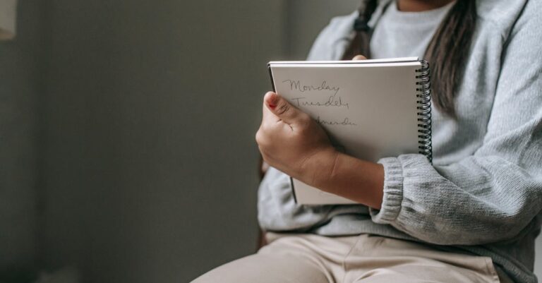 Estudante pensativo escrevendo em caderno com expressão séria em ambiente claro.
